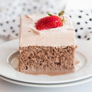 A piece of Chocolate Tres Leches Cake with chocolate whipped cream garnished with a fanned strawberry.