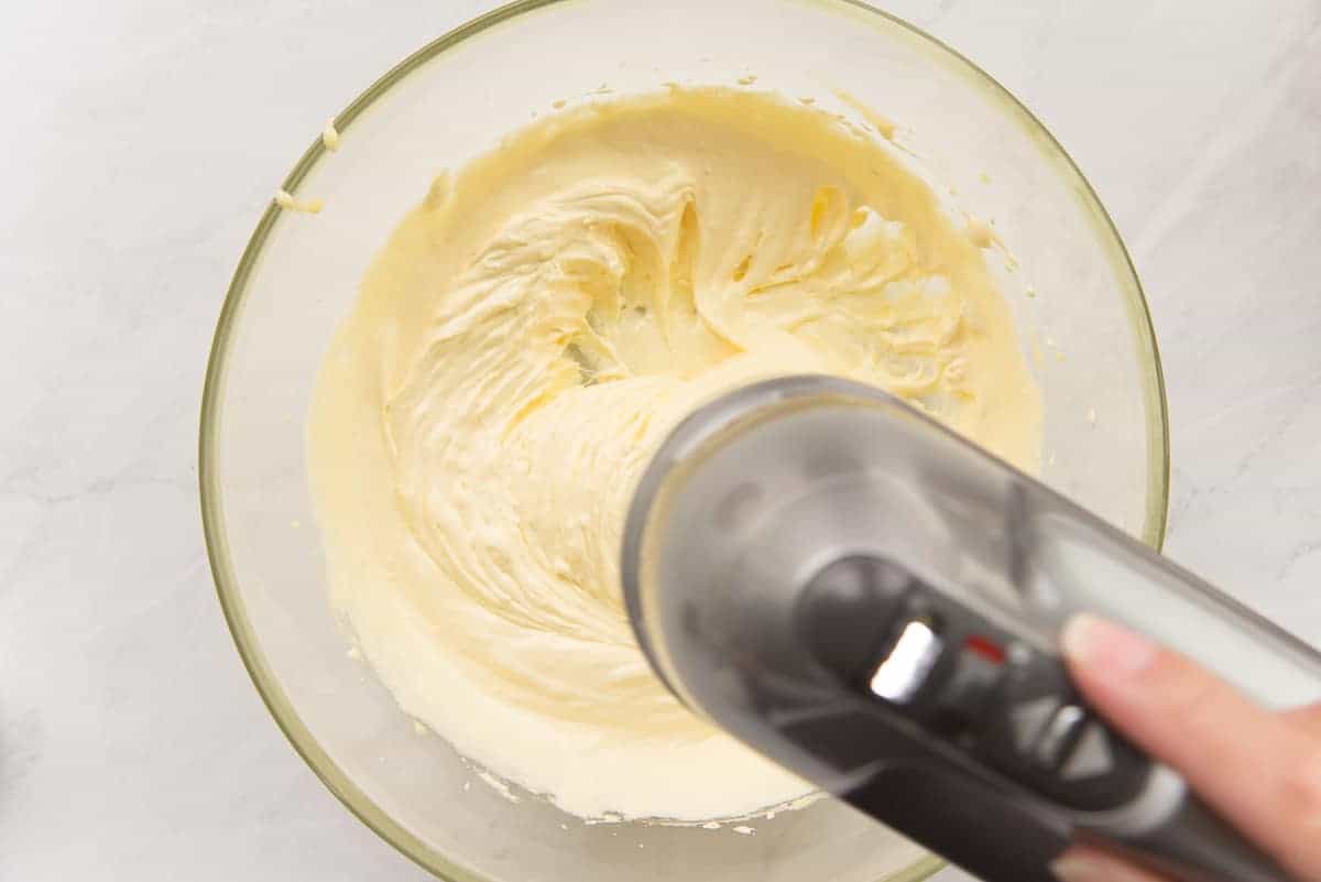 Egg yolks are whipped until lemony yellow in a glass mixing bowl.
