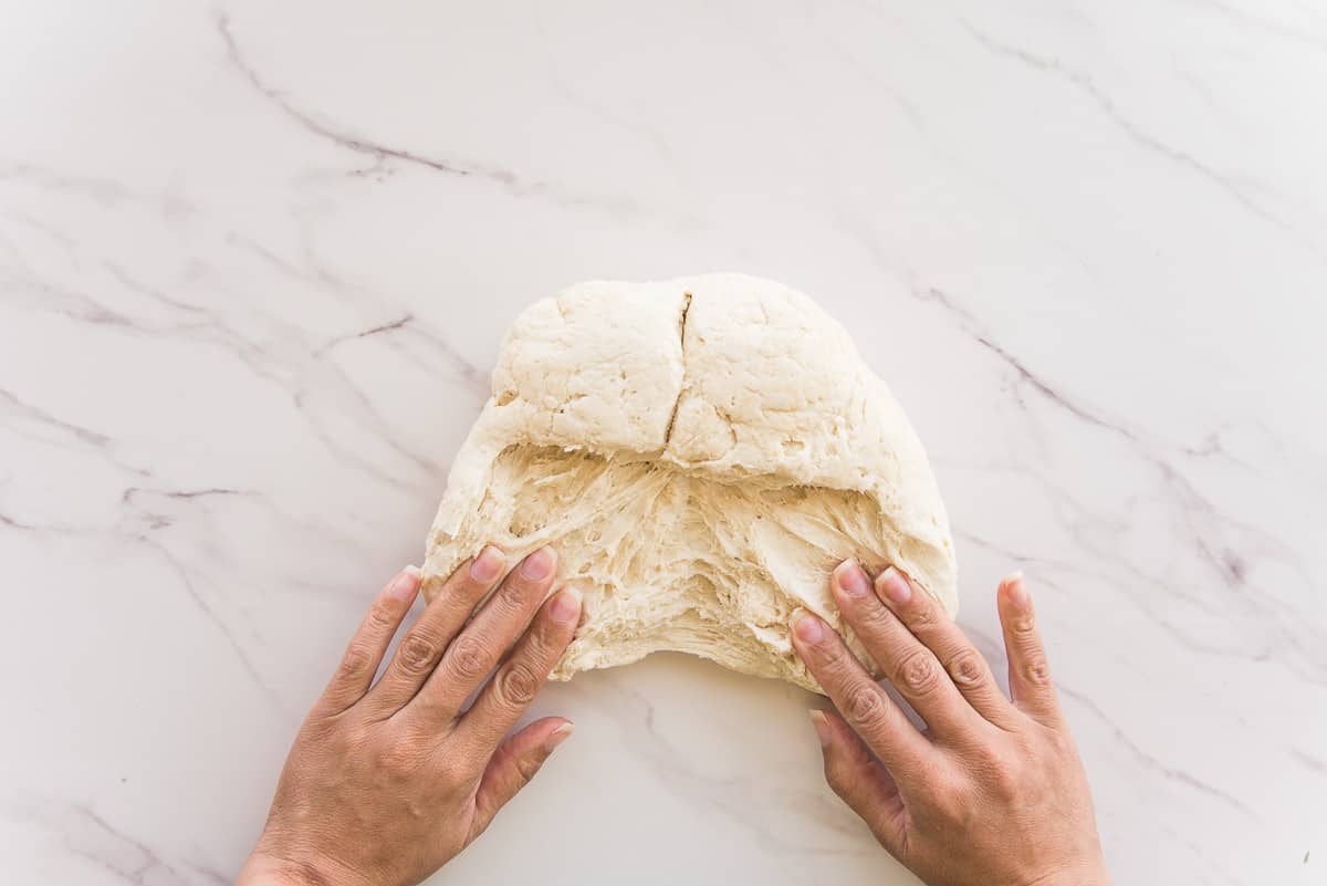 Two hands spread the dough into a square shape.