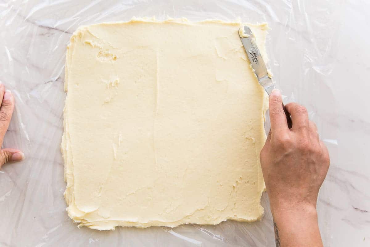 A hand uses an offset spatula to spread the butter flour mixture into a square.