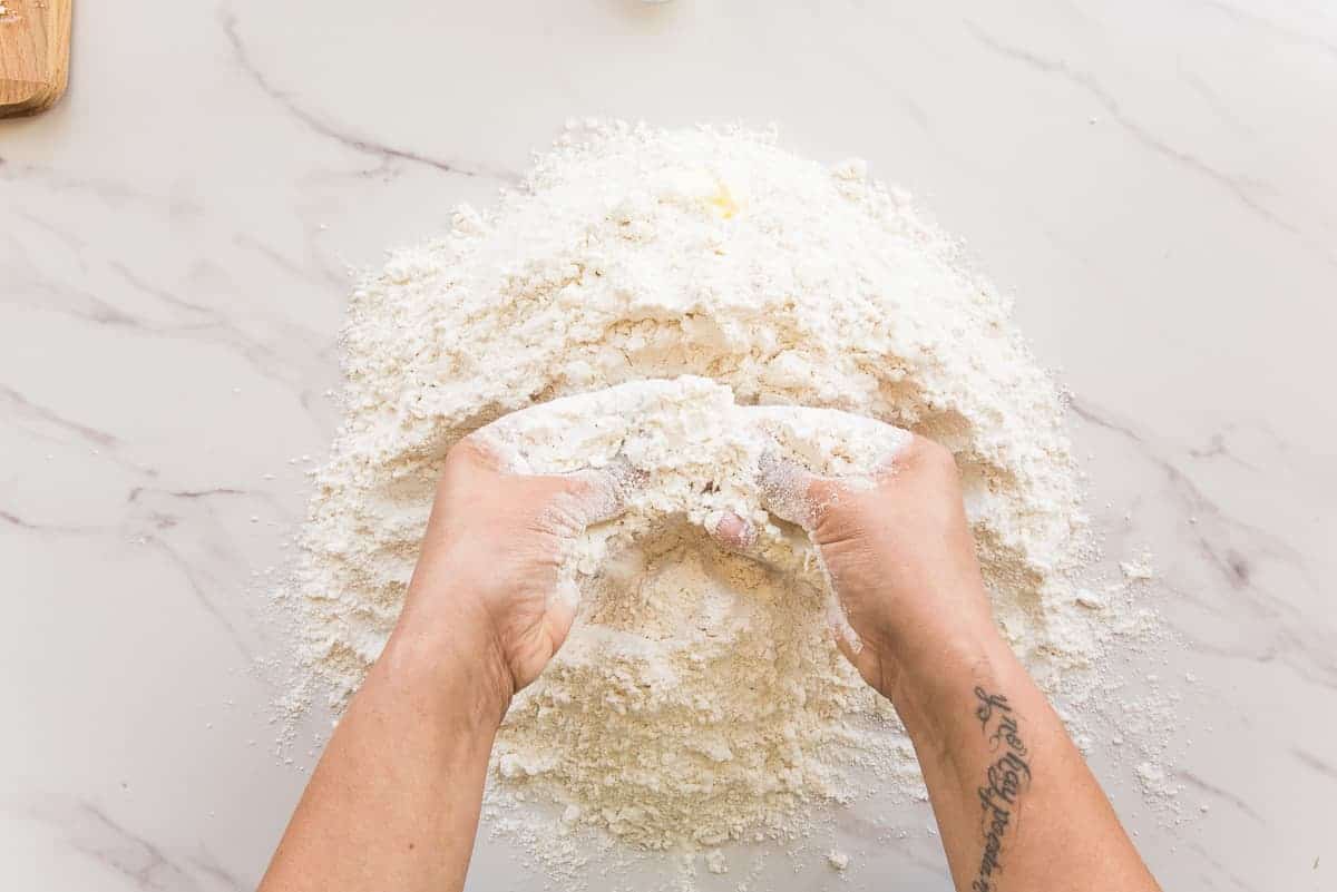 Two hands rub the fat into the flour mixture.