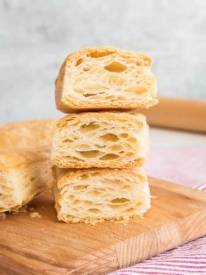 Three pieces of Puff Pastry cut open to reveal their flaky interiors on a wooden cutting board.