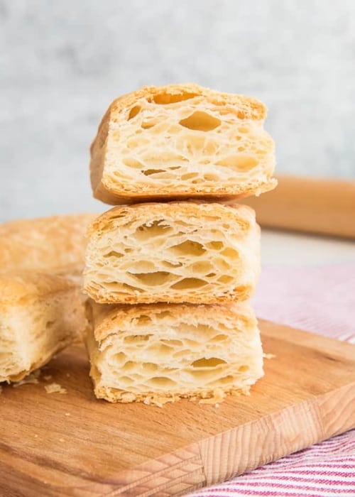Three pieces of Puff Pastry cut open to reveal their flaky interiors on a wooden cutting board.