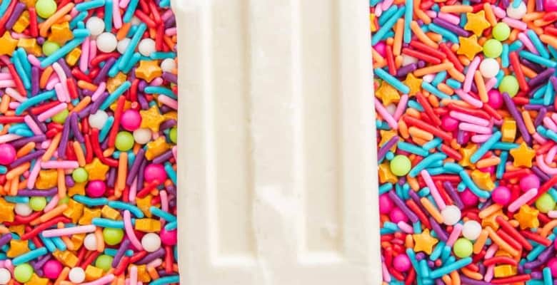A tres leches paletas with a bite removed on a bed of multicolored sprinkles.