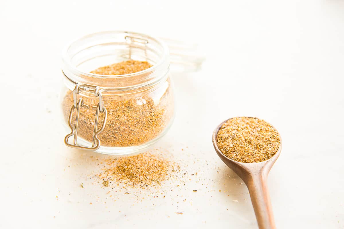 Side view of a glass jar filled with Chicken Seasoning Blend next to a spoon with it.