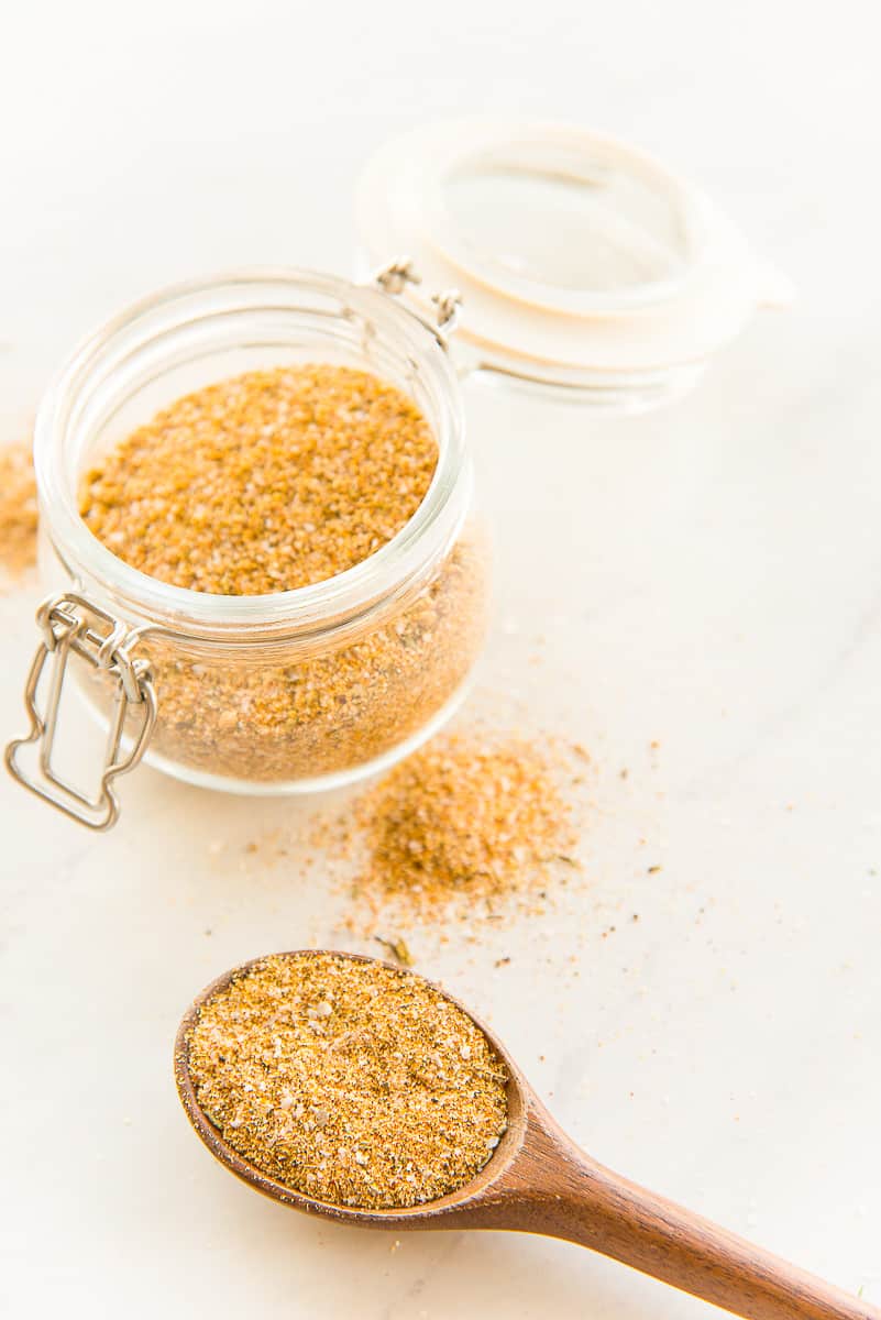 A spoon holds the Chicken Seasoning Blend on it in front of a glass jar filled with the rest of the seasoning blend.