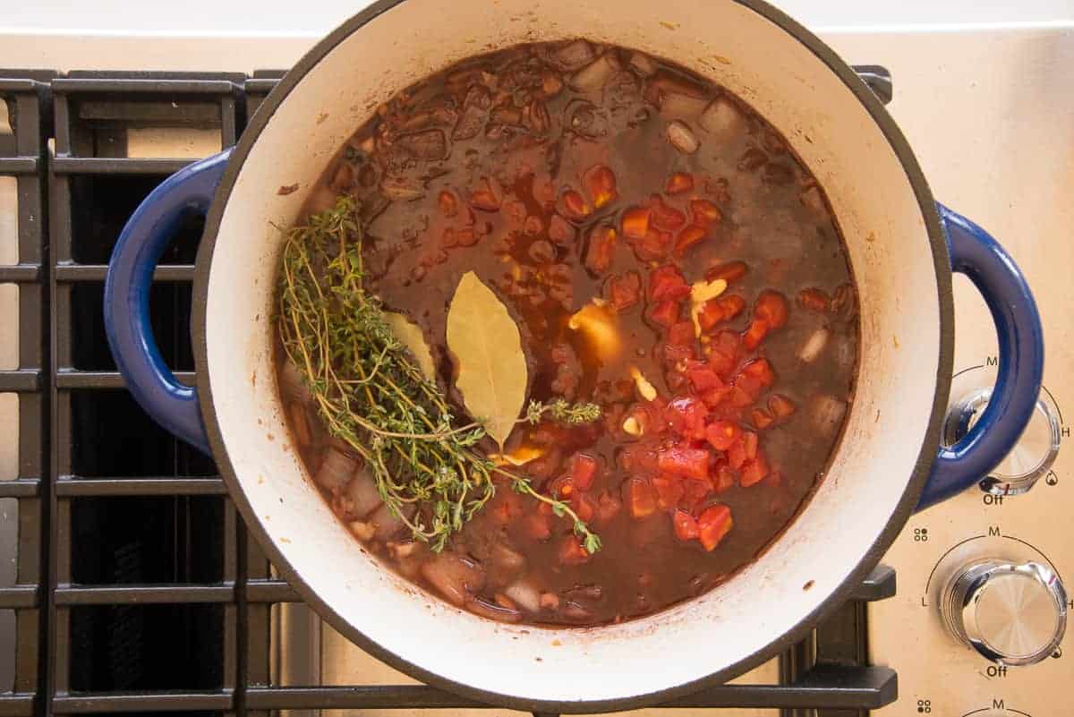 Herbs are added to the rest of the ingredients in the blue Dutch oven.