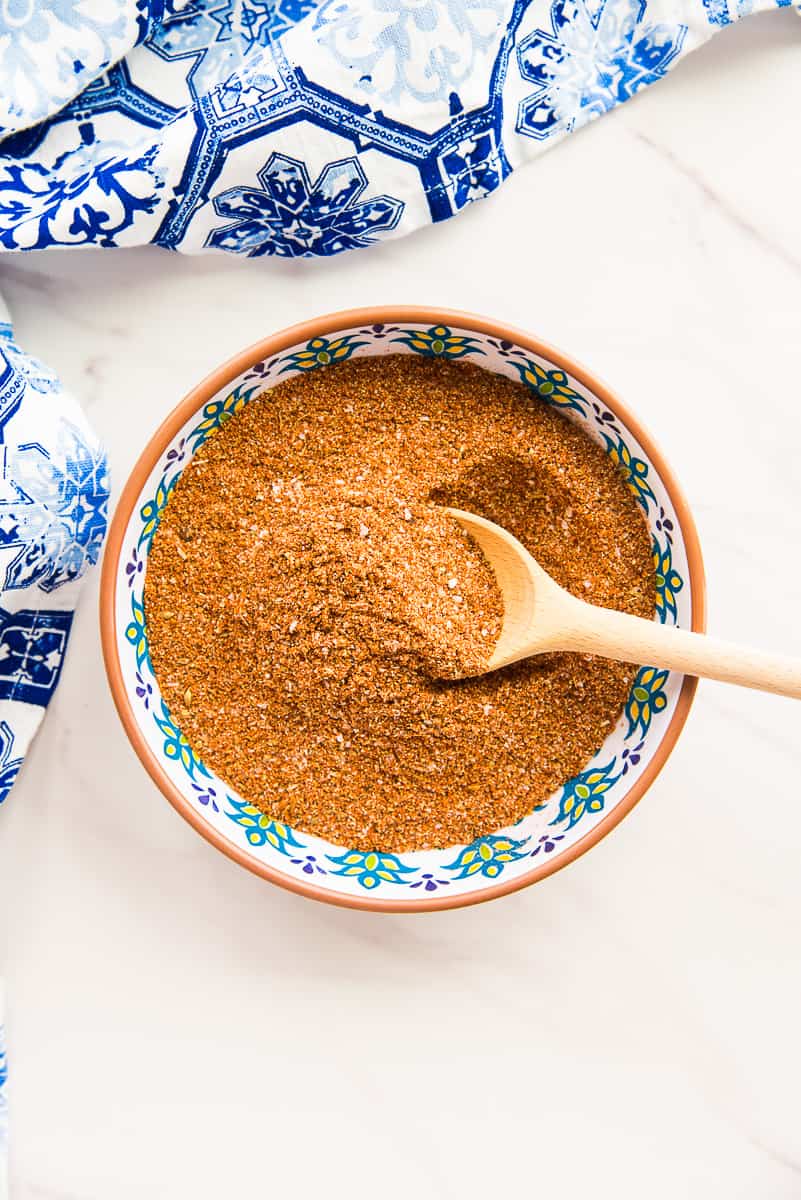 A wooden spoon scoops up some of the Mexican Four Chile Spice Blend in a decorative bowl.