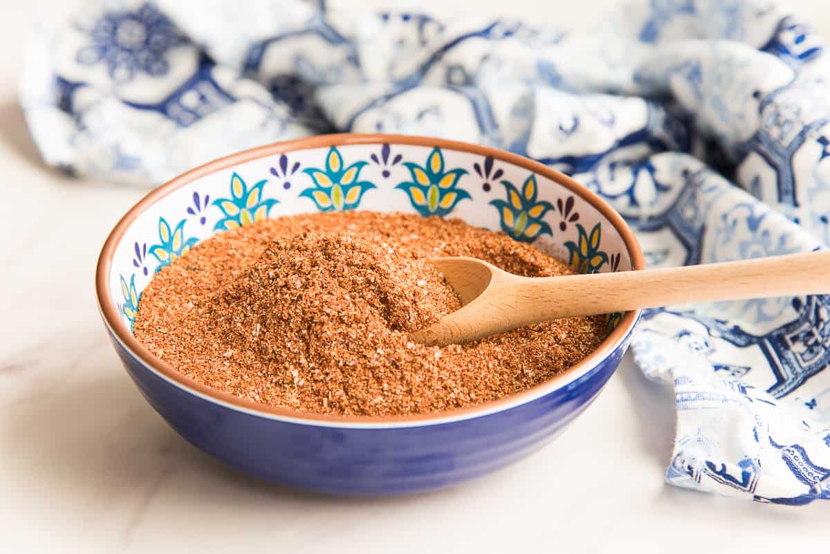 Sideview of a blue, Mexican-style bowl with a wooden spoon scooping up some of the spice blend.