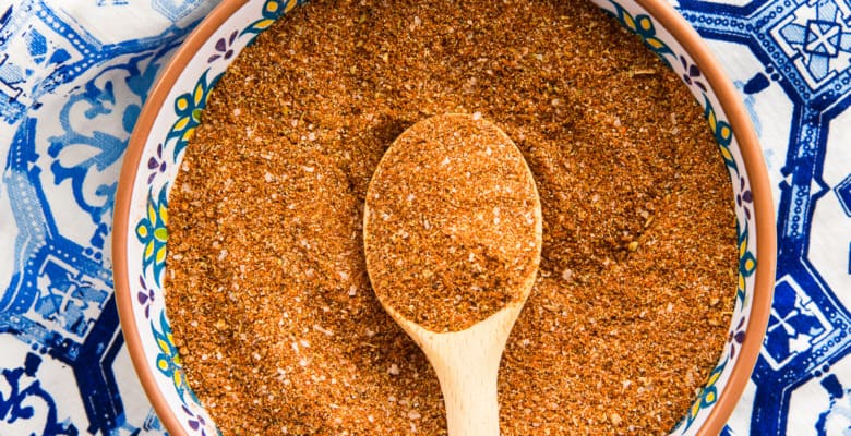 Mexican Four Chile Spice Blend scooped up with a wooden spoon rests on top of the seasoning in a decorative bowl.