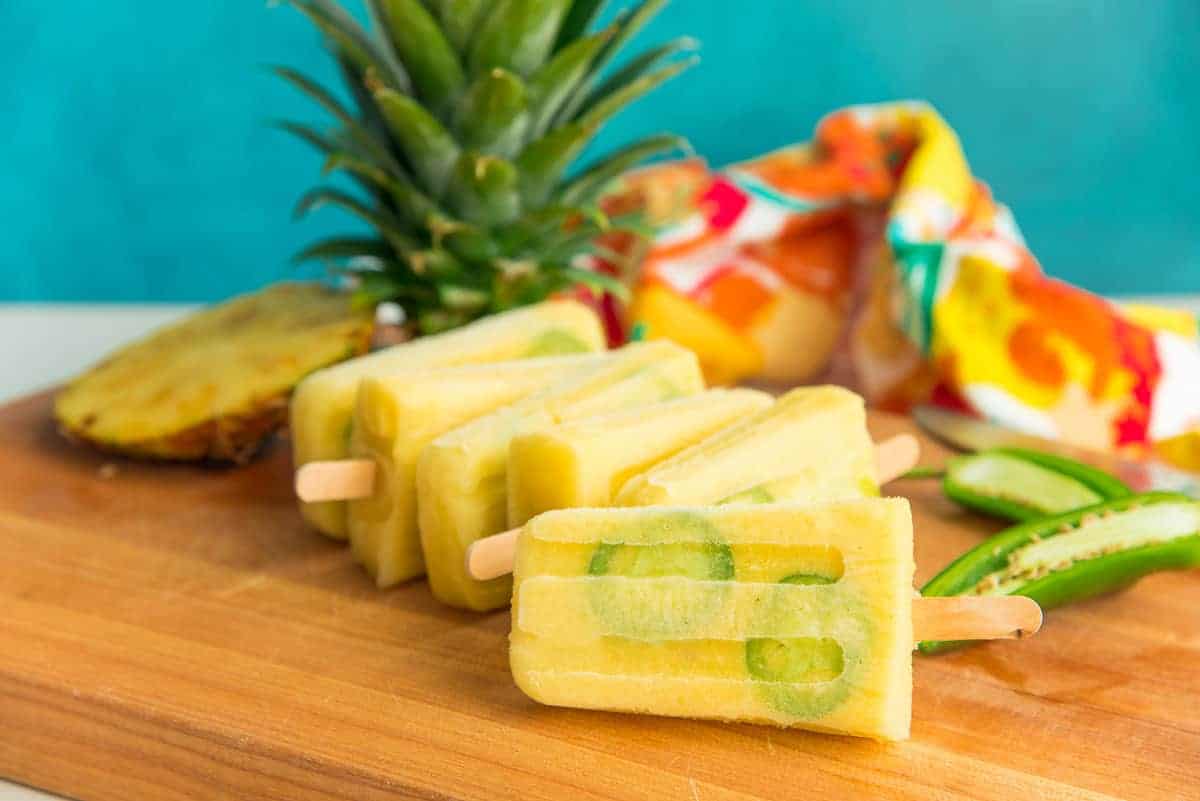 Spicy Pineapple Paletas on their sides stacked in front of each other on a wooden surface.