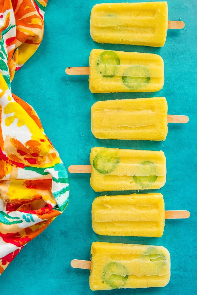 Spicy Pineapple Paletas lined up on a blue surface next to a kitchen towel.