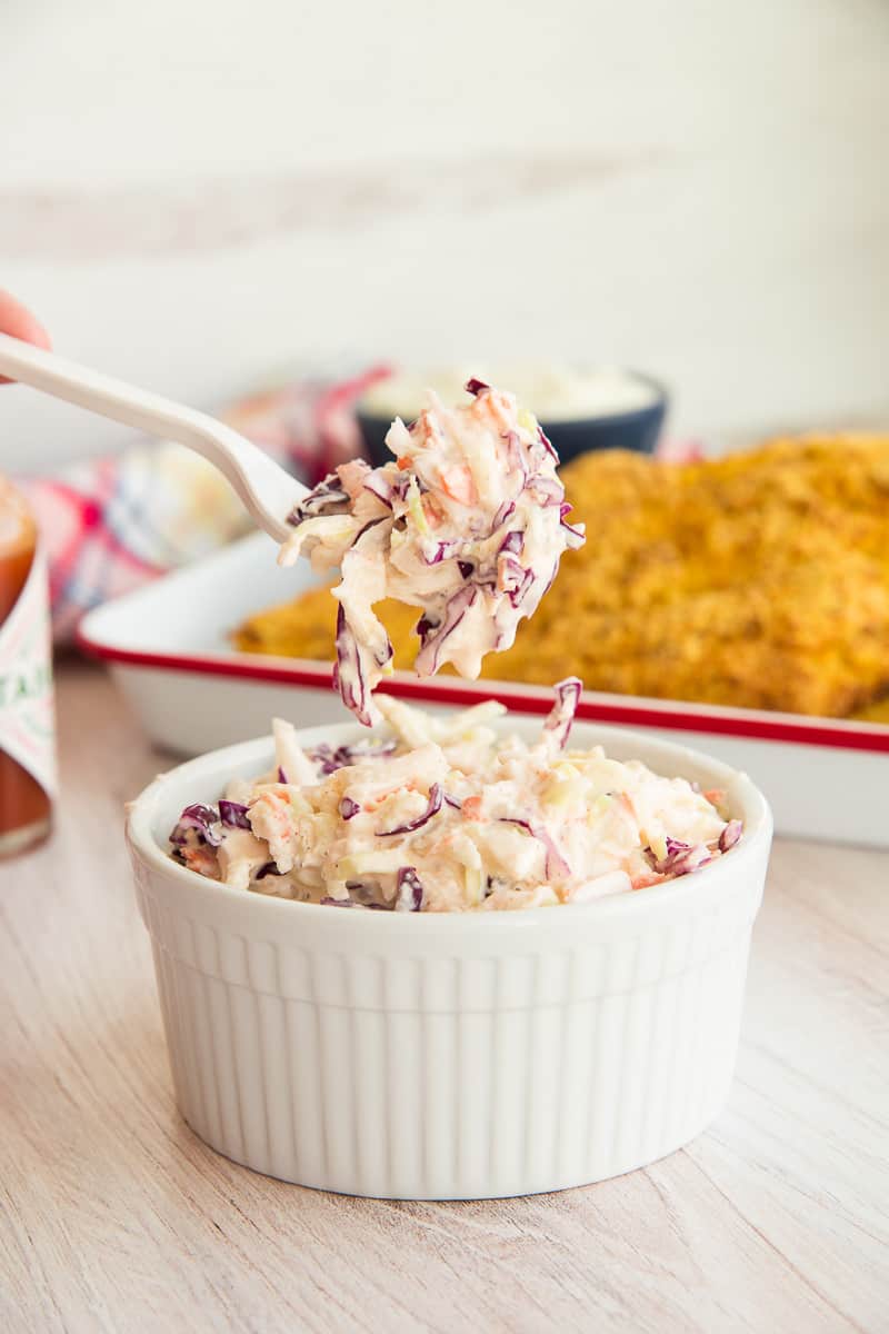 A fork of Homemade Coleslaw is lifted from its ramekin.