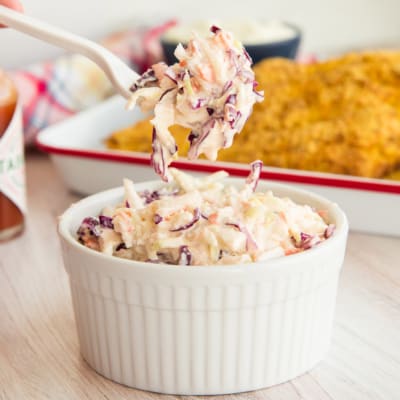 A forkful of Homemade Coleslaw is lifted from a white ceramic ramekin.