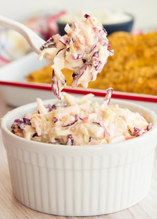 A forkful of Homemade Coleslaw is lifted from a white ceramic ramekin.