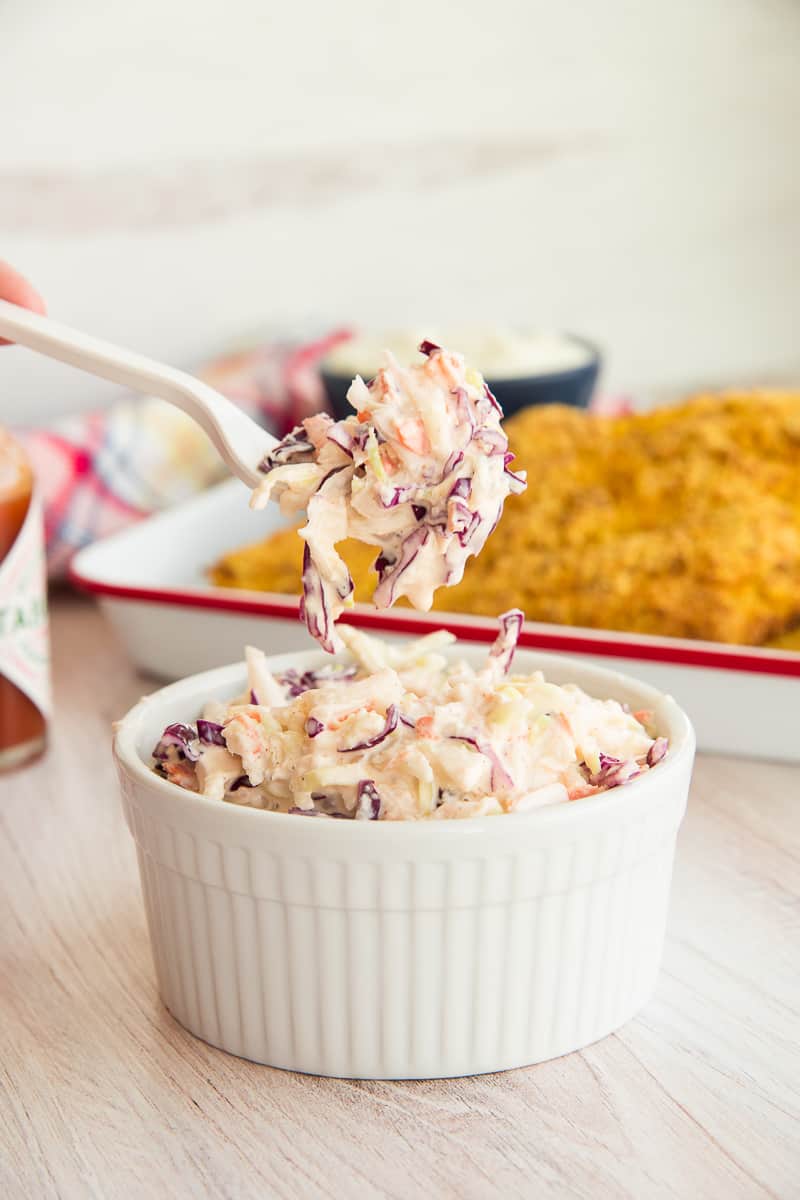 A fork of Homemade Coleslaw is lifted from the rest of the coleslaw in a white ramekin.