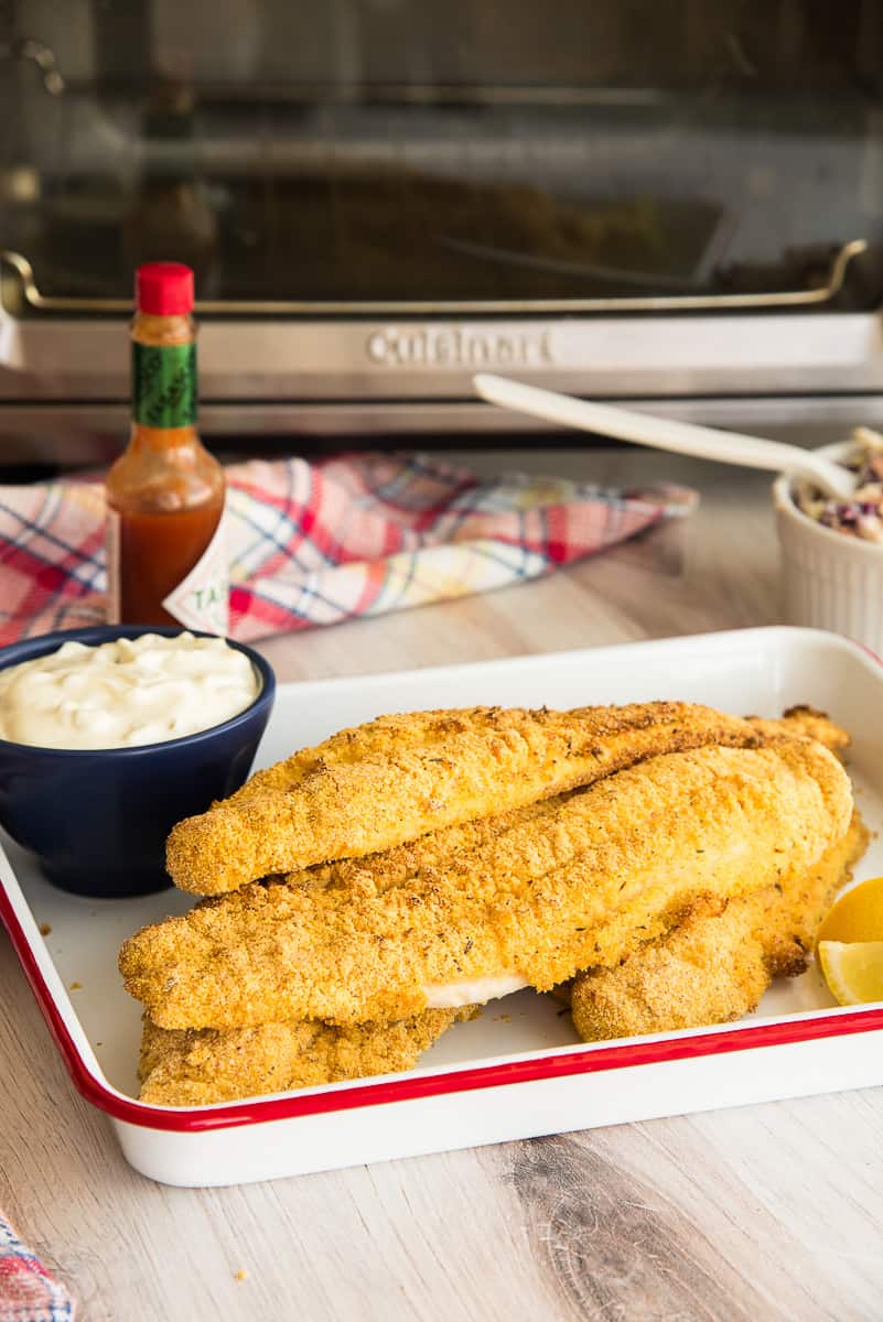 Air Fried Southern Catfish filets stacked on a white tray in front of an air fryer.