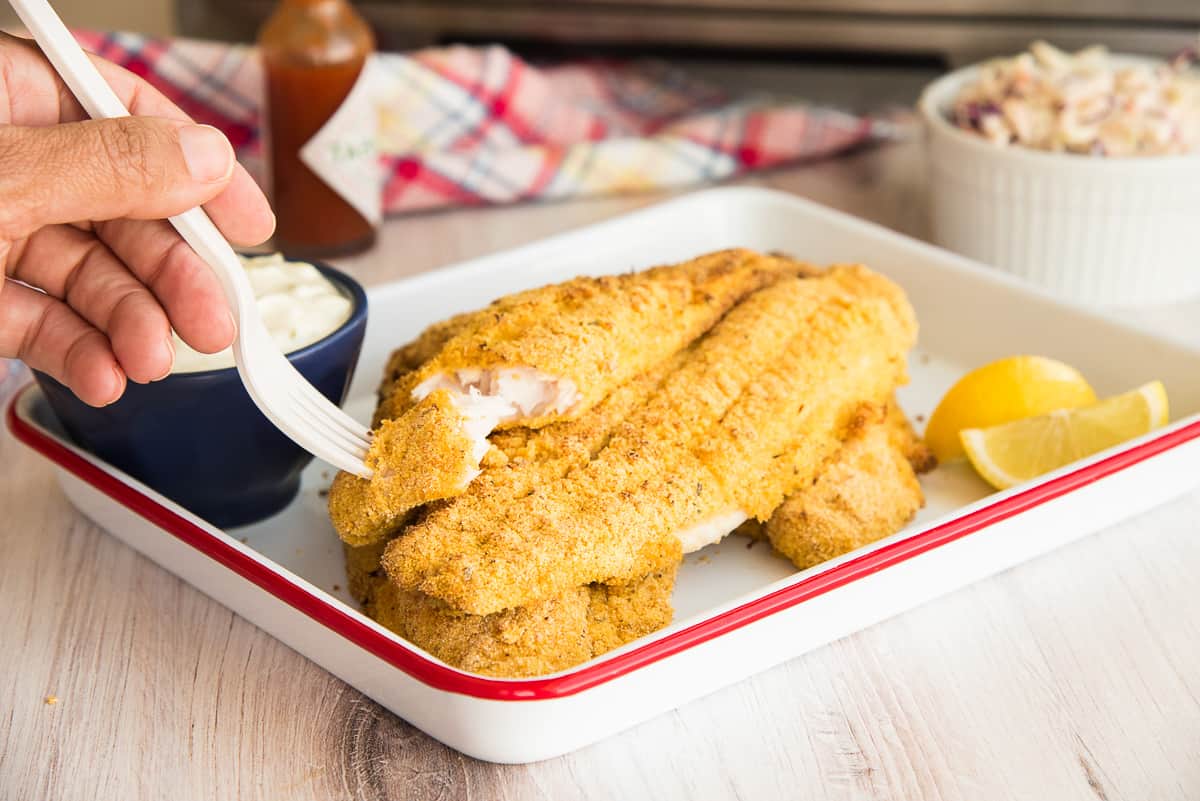 A hand uses a fork to pull a piece of Air Fried Southern Catfish from the filet.