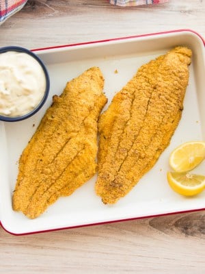 Two Air Fried Southern Catfish filets on a white tray with tartar sauce and lemon wedges.