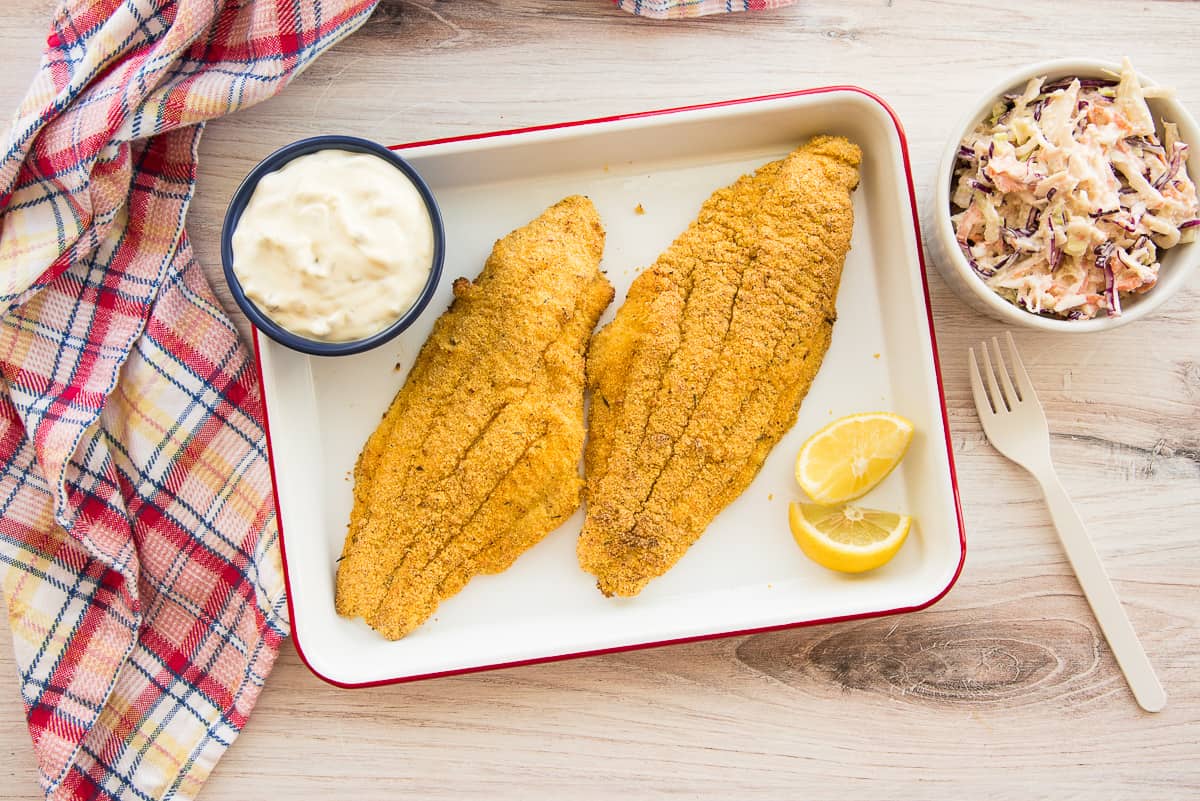 Two Air Fried Southern Catfish filets on a white tray with tartar sauce and lemon wedges.