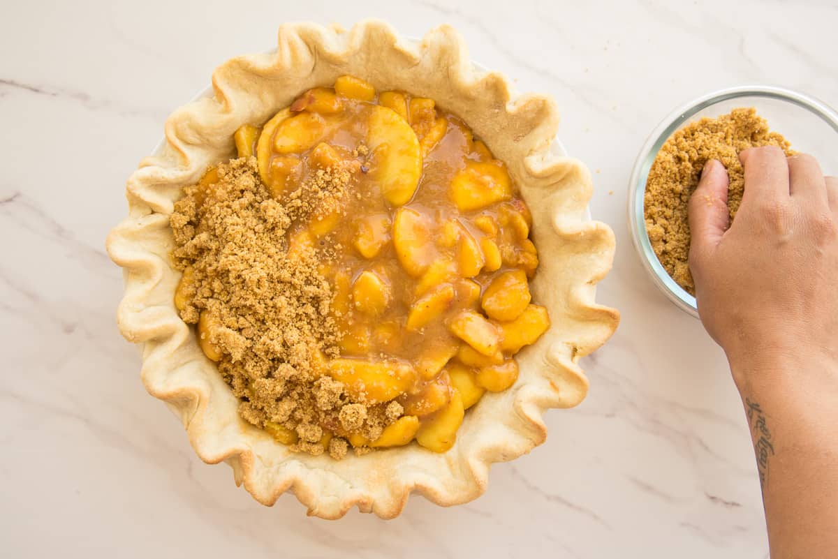 A hand scoops the cornmeal crumble topping onto the pie filling before it's baked.