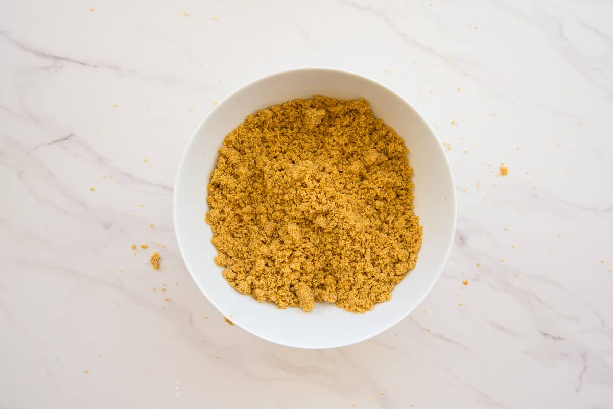 The cornmeal crumble is mixed to form crumbs in a white ceramic mixing bowl.