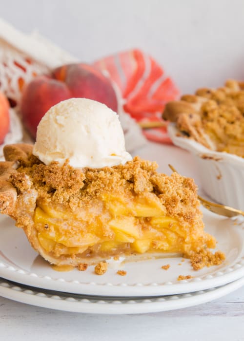 A slice of Peach Pie with Cornmeal Crumble Topping topped with vanilla frozen custard on a white plate.