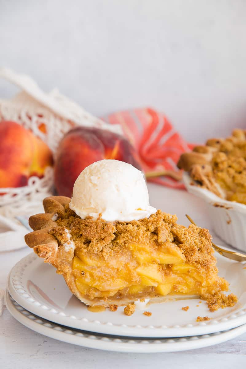 A slice of the Peach Pie with Cornmeal Crumble Topping served a la mode on a white plate.