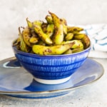 A blue bowl of Spicy Garlic Edamame on a blue plate.