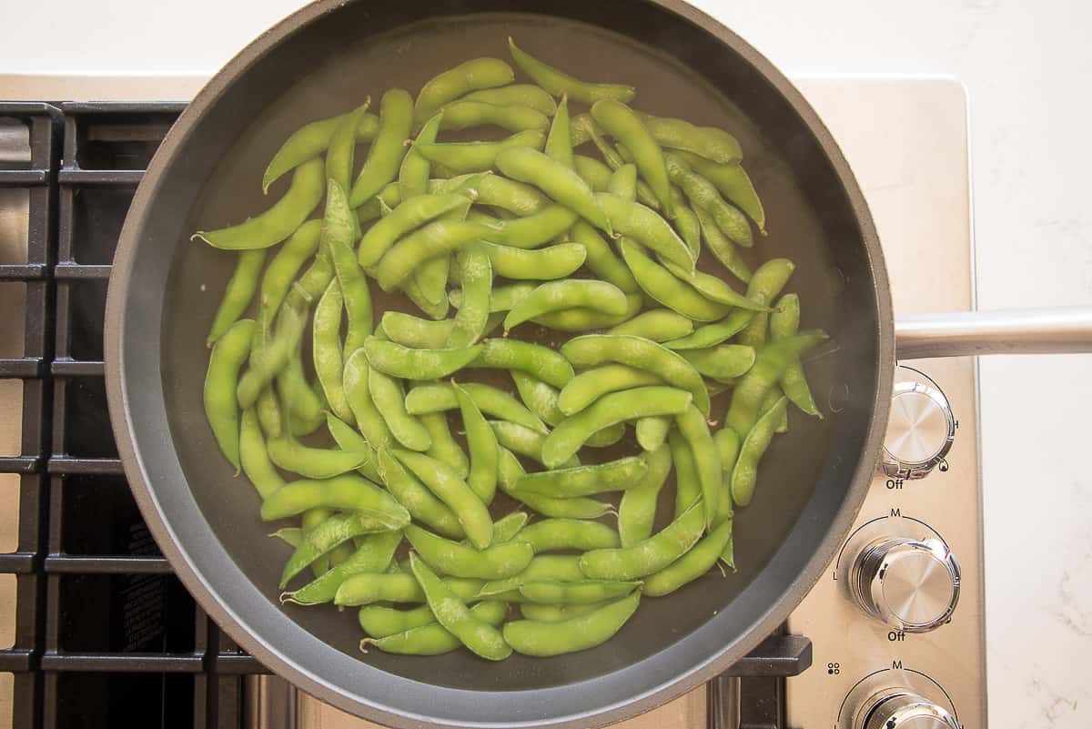 The edamame are added to salted water in a frying pan.