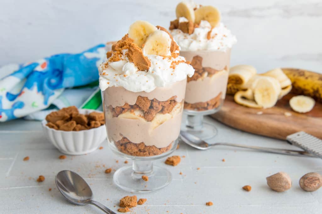 Two glasses of Vegan Banana Pudding garnished with whipped cream, crushed cookies, and sliced bananas.
