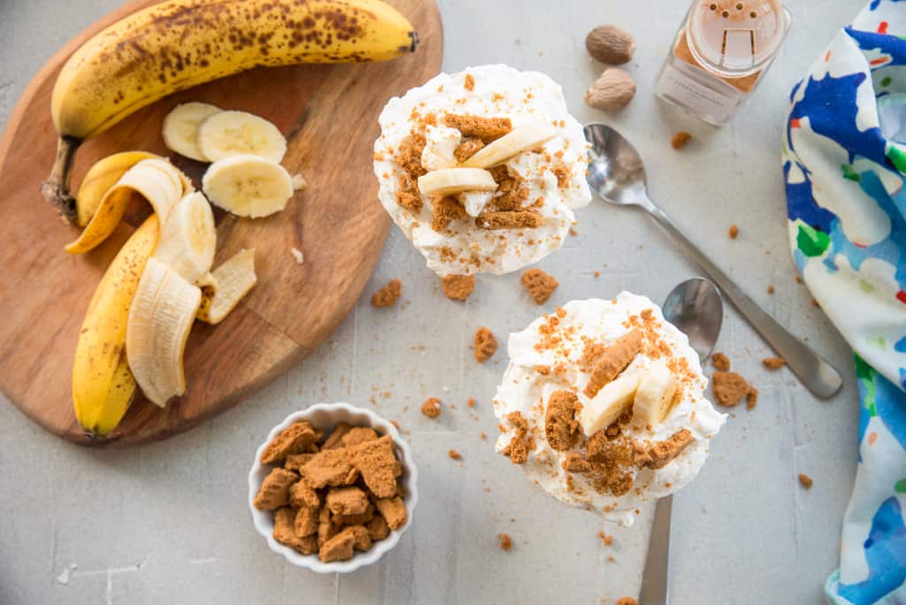 The tops of two glasses of Vegan Banana Pudding next to a cutting board with sliced and a whole banana.