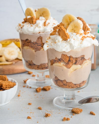 Two goblets of Vegan Banana Pudding garnished with whipped topping and crushed cookies and banana slices.