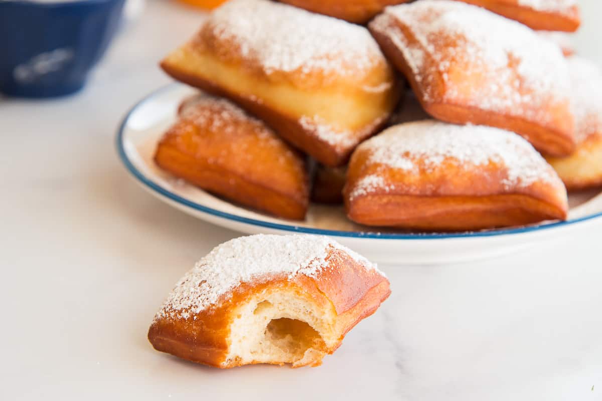 A bitten-into Beignet sits in front of a plate of Beignets.