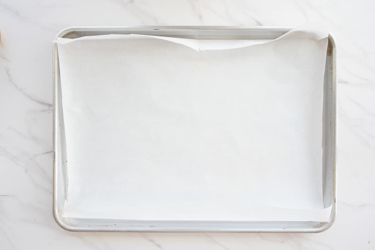 A piece of parchment paper is used to line a silver sheet pan.