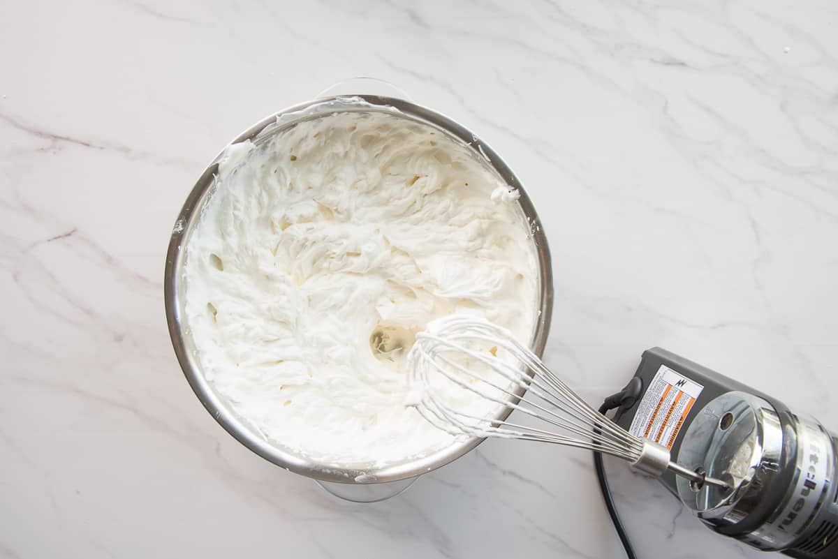 An electric mixer after whipping heavy cream in a silver bowl.