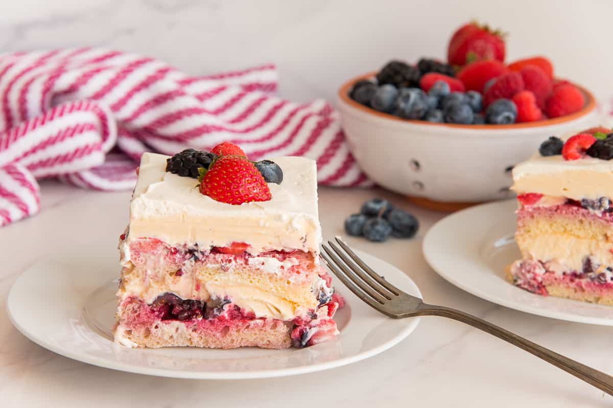Two servings of Berry Tiramisu on white plates in front of a bowl of fresh berries.