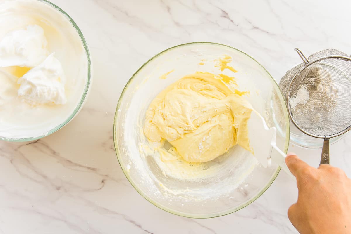 Cake flour is folded into the whipped egg yolks in a clear mixing bowl.
