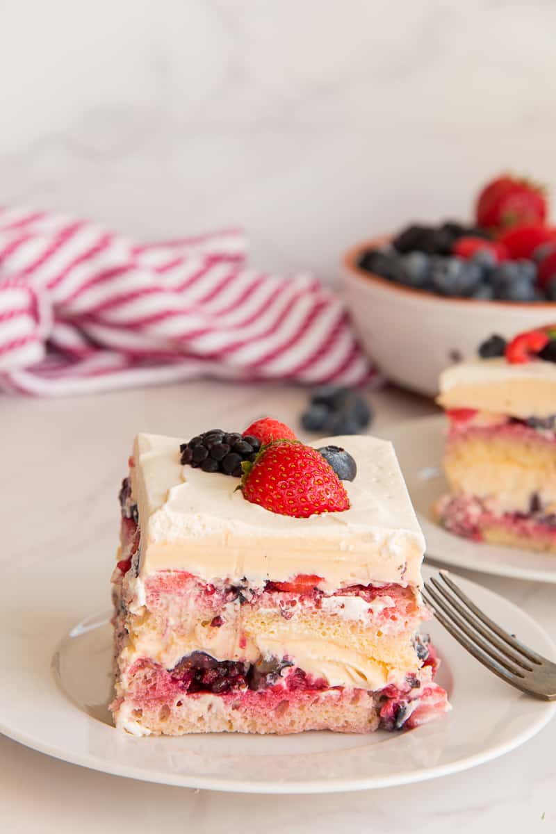 A piece of Berry Tiramisu on a white plate in front of a red and white striped kitchen towel.