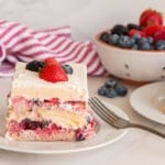 Two pieces of Berry Tiramisu on white plates in front of a colander filled with fresh berries.