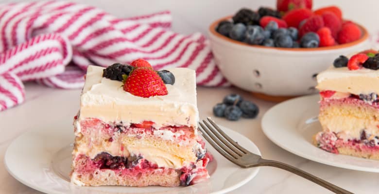 Two pieces of Berry Tiramisu on white plates in front of a colander filled with fresh berries.