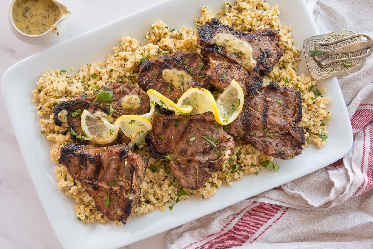 Garlic Herb Grilled Lamb Chops on a bed of farro next to a small pitcher of sauce.