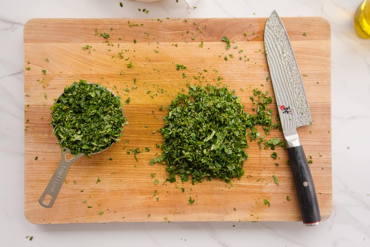 The chopped herbs on a wooden cutting board next to a knife.