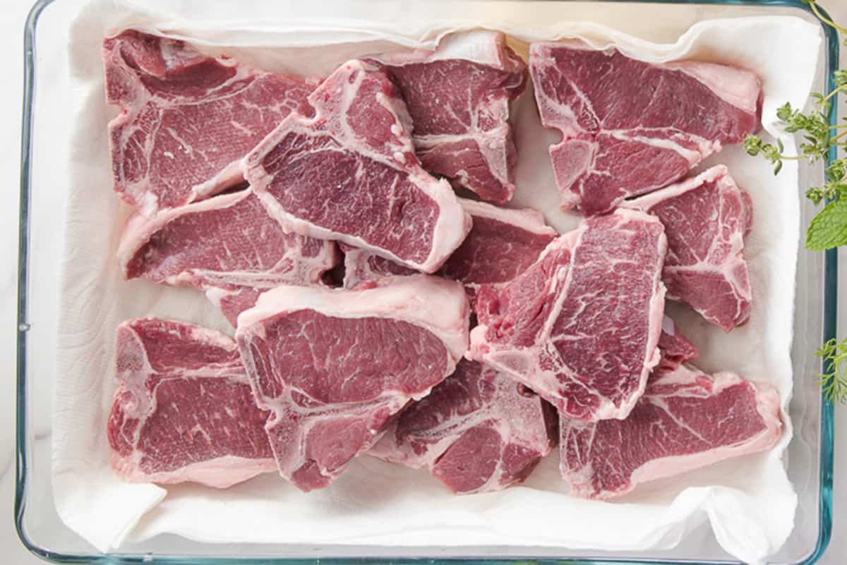 Close up of lamb loin chops in a clear glass baking dish.