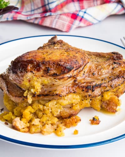 Pork Chops with Mofongo Stuffing on a white plate with a blue rim next to a fork and steak knife.
