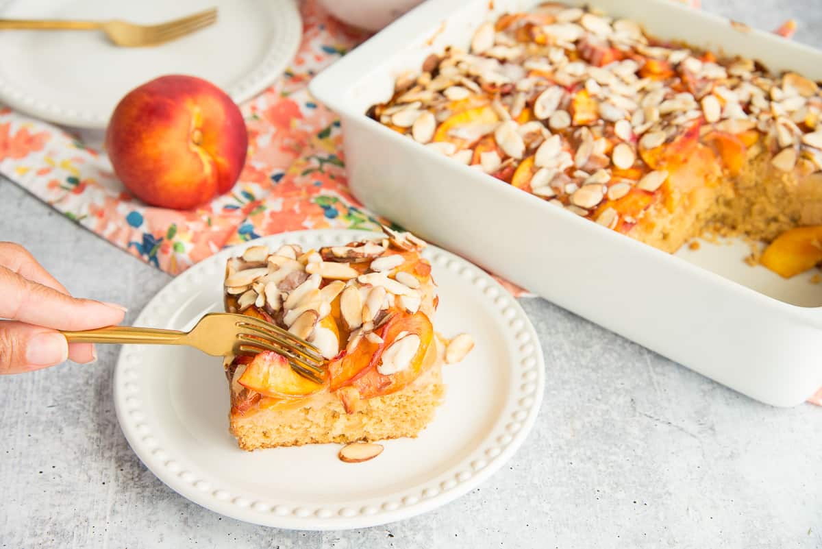 A fork is pressed into a slice of Nectarine Almond Coffee Cake on a white plate.