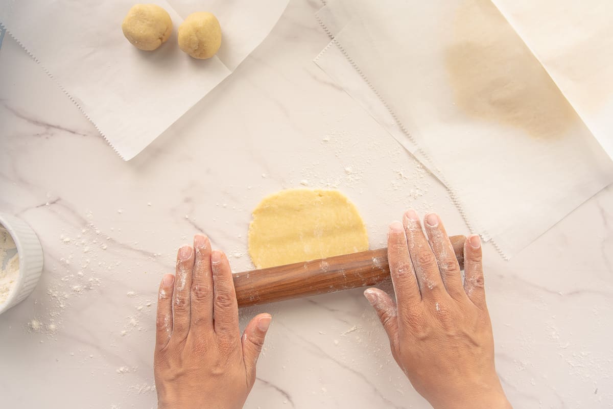 Hands uses a wooden rolling pin to roll the balls of dough into a disc.