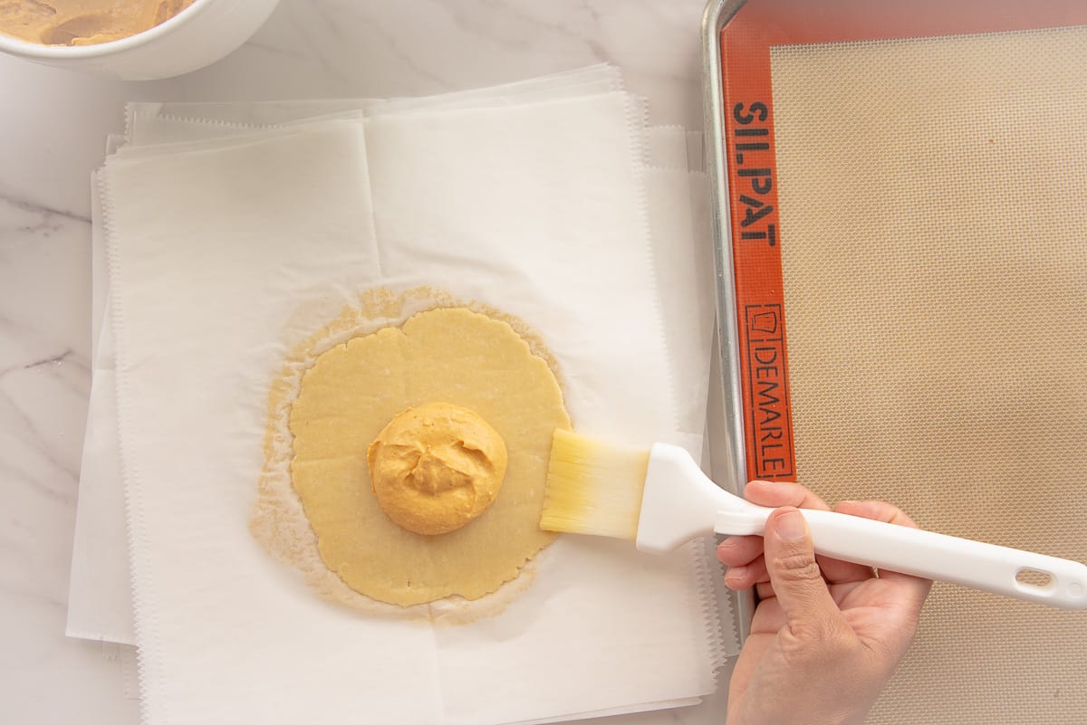 A hand brushes egg wash onto the edges of the dough with a pastry brush.