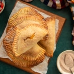 A stack of Pumpkin Cheesecake Empanadas on a wooden board next to a bowl of spiced sugar.