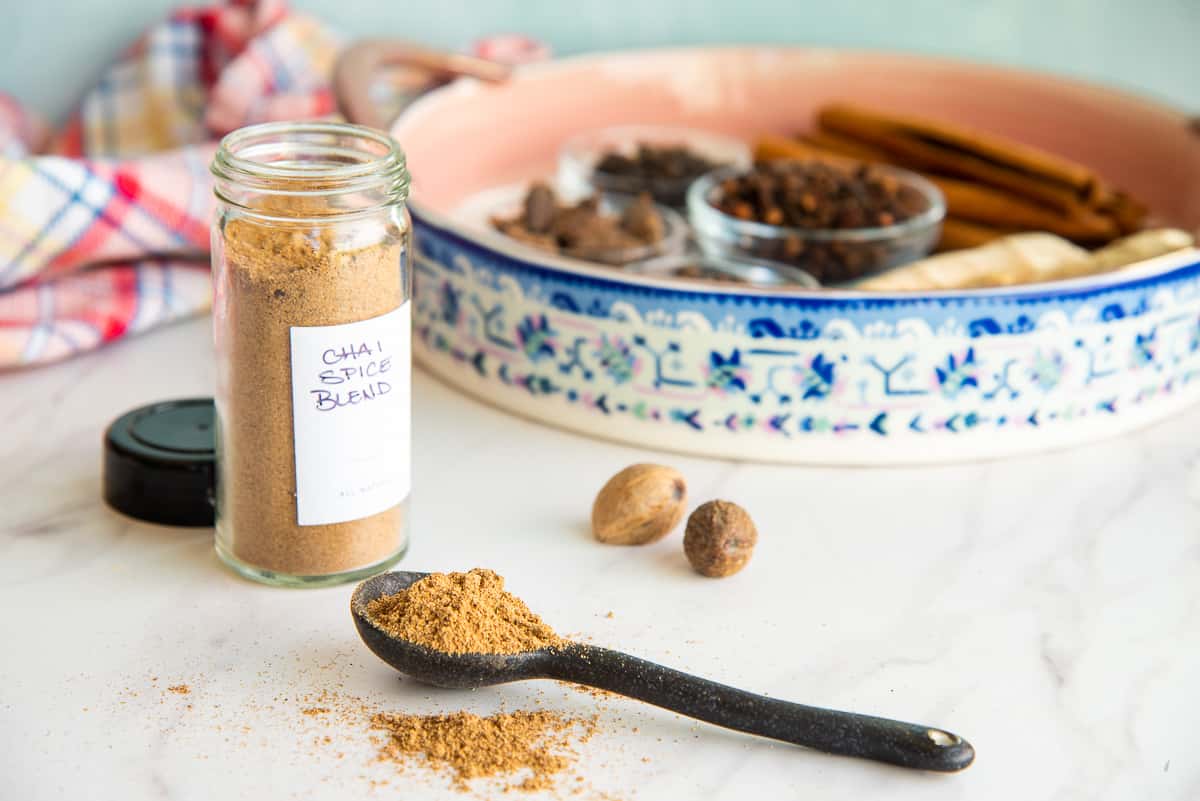 Chai Spice Blend on a black spoon in front of a platter with the spices used in the recipe.